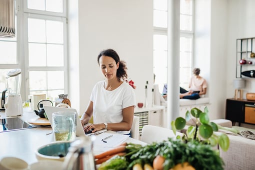 woman doing remote work woman doing remote work on laptop in kitchen, with another person working in the background
