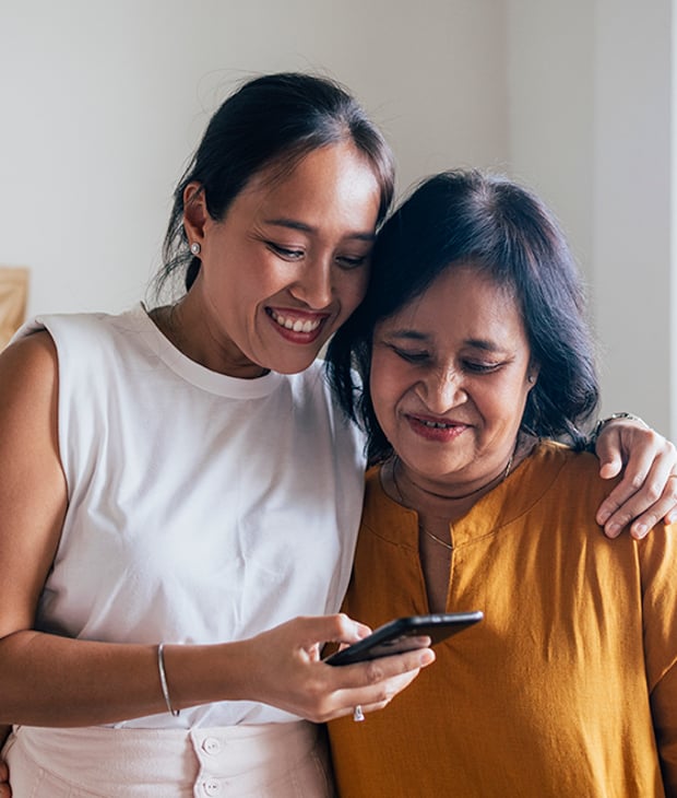 Image of woman with her arm around her mother, looking at a mobile phone screen