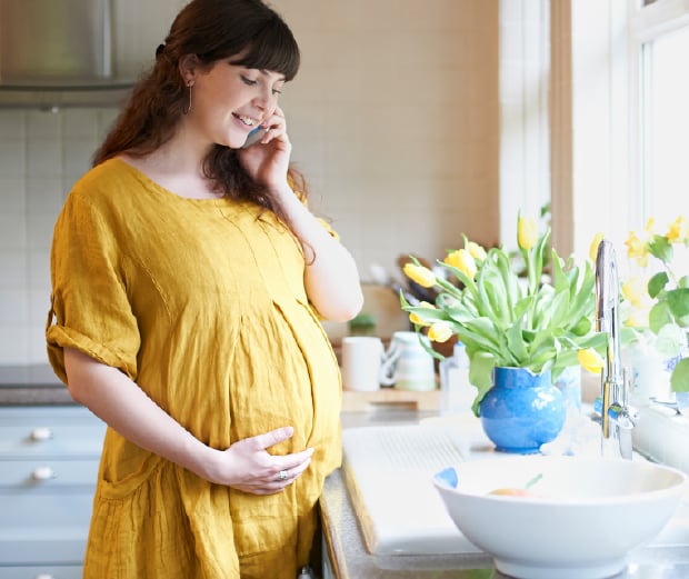 Pregnant women on phone standing in bright home kitchen