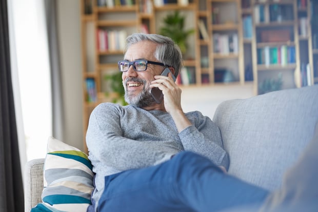 Mature man on the phone sitting on couch at home looking out of window