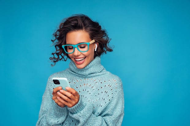 1280369513 Beautiful woman standing in front of blue background with smart phone